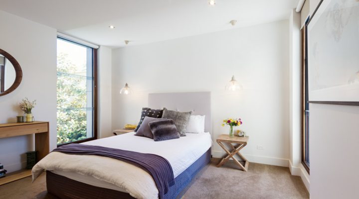 Bright and airy modern bedroom featuring a minimalist design with a comfortable bed, wooden accents, and large windows that provide ample natural light.