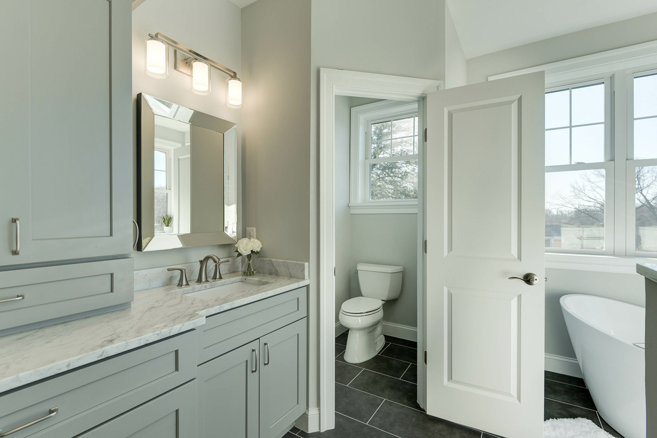 Bright and spacious bathroom with a glass-enclosed shower, blue vanity with double sink, and intricate tile flooring.