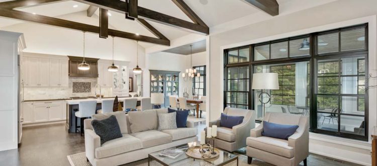 Spacious open concept living area featuring high ceilings with wooden beams, a large seating arrangement, and a modern kitchen with white cabinetry, all bathed in natural light.