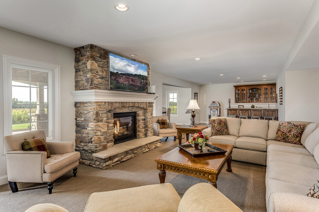 Cozy living room featuring a large sectional sofa, a stone fireplace, and rustic wooden furniture, providing a warm and inviting family space.