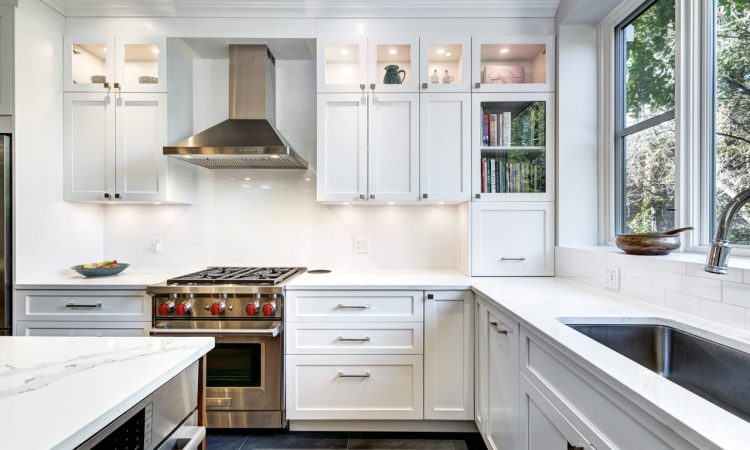 A bright modern kitchen with white cabinetry, marble countertops, and stainless steel appliances, complemented by natural light from surrounding windows.