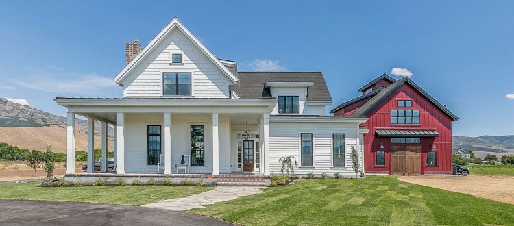 Front view of a large family home with classic white siding and a distinctive red barn-style garage, set against a backdrop of mountainous terrain.