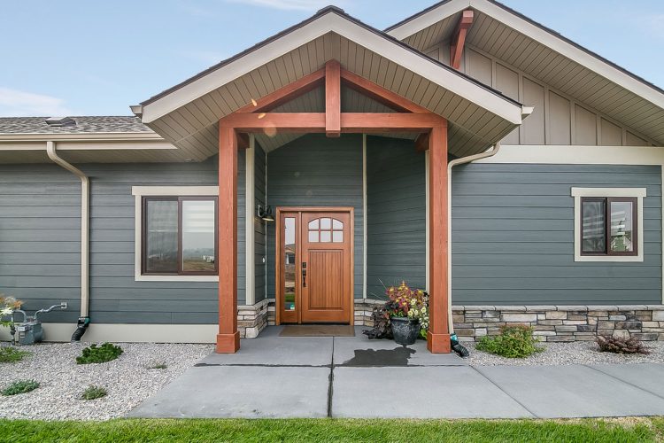 Close-up view of a home's entryway with a wooden door and a covered porch supported by wooden beams, complemented by a landscaped front area.