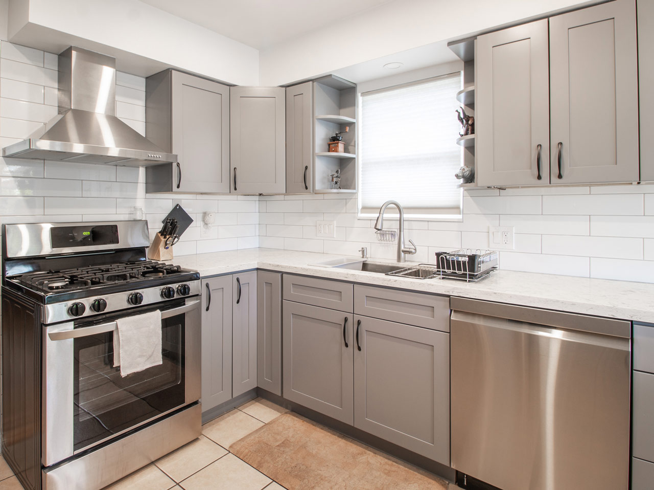 A compact modern kitchen featuring gray cabinetry, white subway tile backsplash, and stainless steel appliances, providing a functional and stylish cooking space.