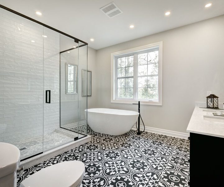 Elegant bathroom showcasing a freestanding bathtub, large glass shower, and distinctive black and white patterned floor tiles, complemented by a serene window view.