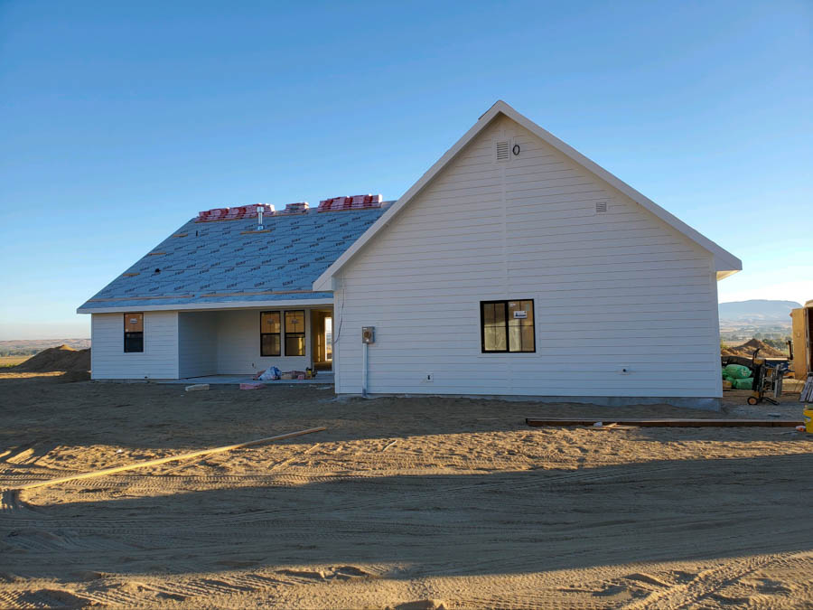 View of a newly constructed single-story residential home with white siding and a partially completed roof in a suburban setting.