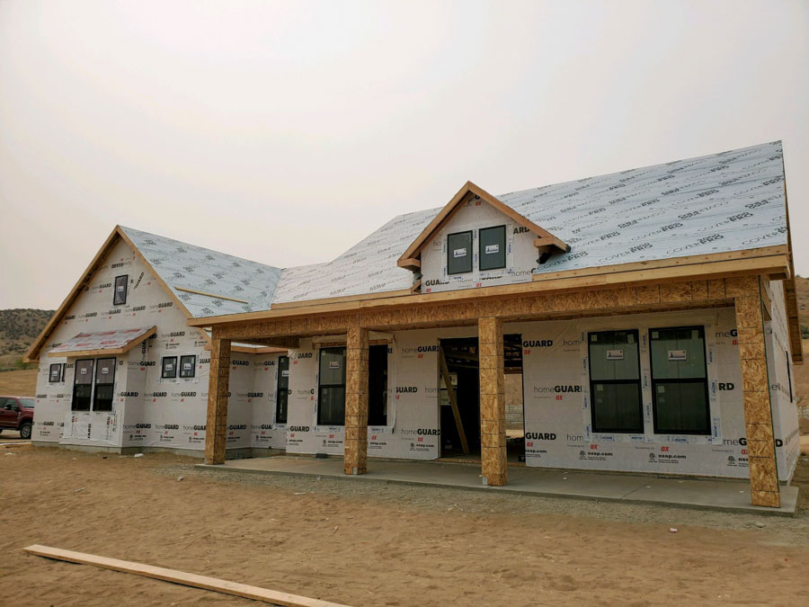 Construction phase of a residential home with wooden framing under a clear sky, surrounded by scaffolding and covered in protective house wrap.