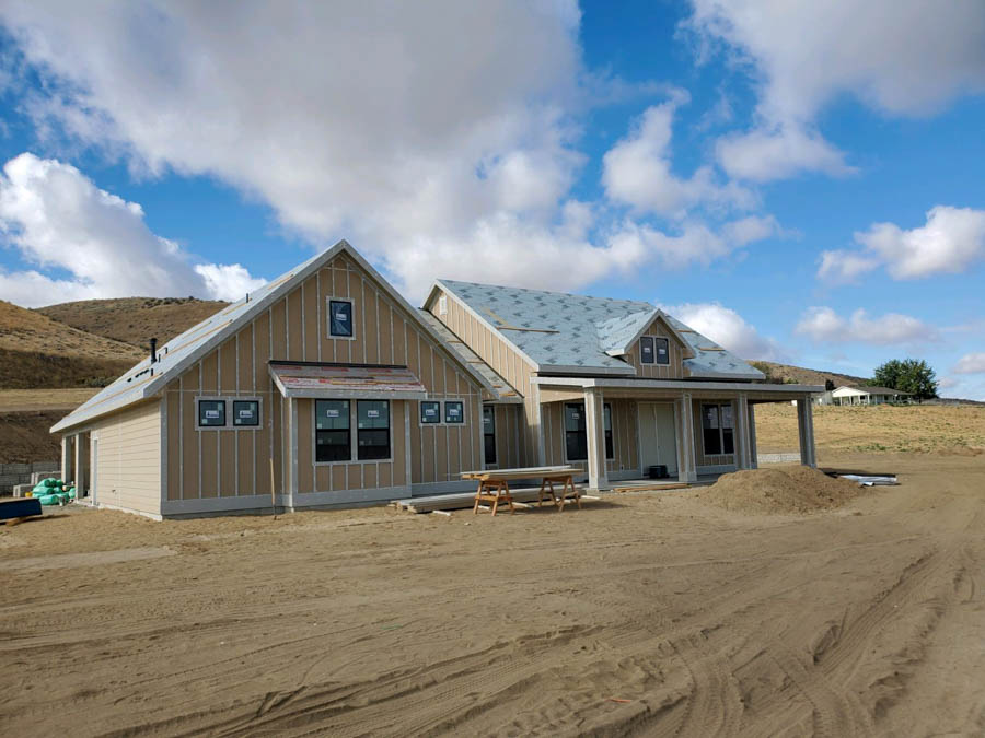 New home construction in a rural area with exposed frames and house wrap, set against a backdrop of rolling hills and a cloudy sky.