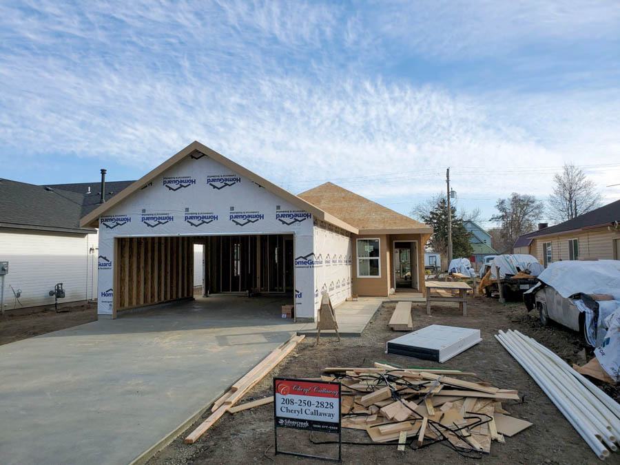 Exterior view of a new home under construction with visible wooden frames and house wrap, showing various building materials scattered around.