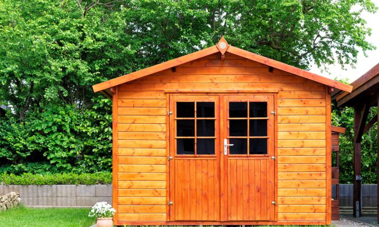 A quaint wooden garden shed with a red door and windows, situated in a lush green backyard, ideal for garden storage or a small workshop.